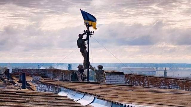Żołnierz zawiesza ukraińską flagę na antenie na dachu