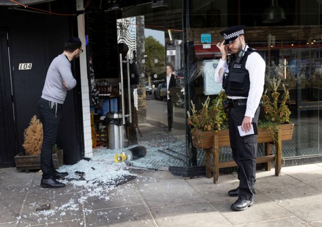 Un joven judío y un policía observan una vitrina rota en un establecimiento judio en el norte de Londres