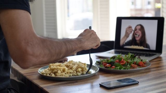 Un hombre y una mujer cenando a través de una videollamada.