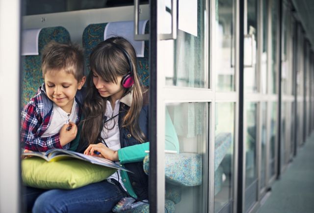 A boy and a girl, on a train, listening to headphones