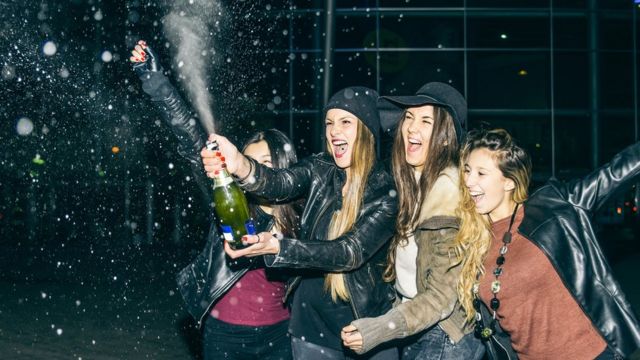 Cuatro mujeres descorchando una botella de champagne.