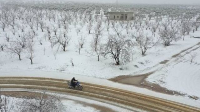 رجل يستقل دراجة بخارية على طريق وسط مزارع غطتها الثلوج