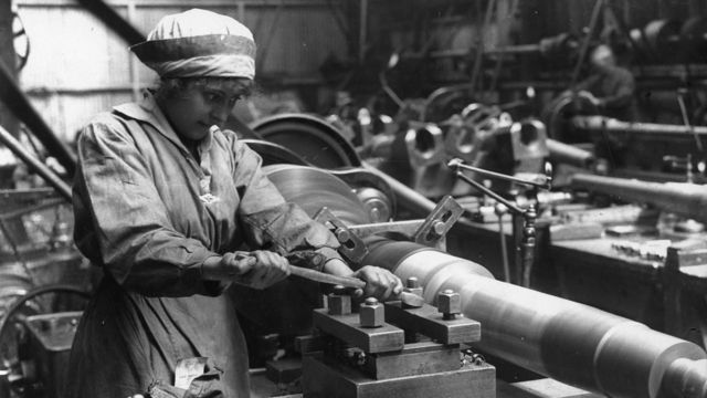 Foto em preto e branco mostra mulher operando maquinário pesado em fábrica de munições