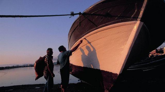 Dos hombres pintan un barco en Cambados.