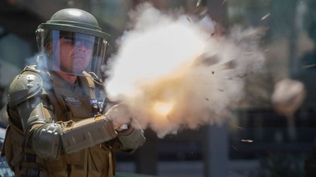 policía con casco lanza gas lacrimógeno
