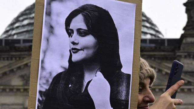 A woman takes a selfie as she holds a portrait of Mahsa Amini during a demonstration in front of the German lower house of parliament on International Women's Day, on 8 March 2023