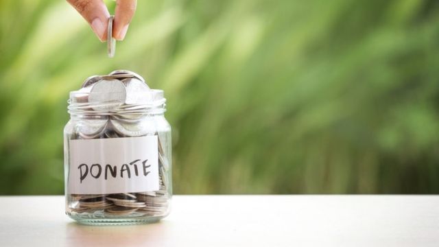Una persona colocando una moneda en un frasco de donaciones