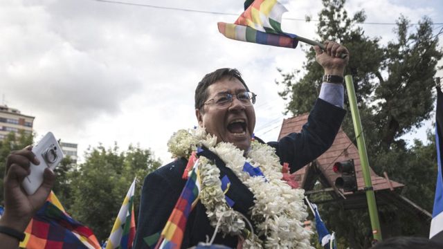 Luis Arce segura uma bandeira da Bolívia e enquanto grita algo