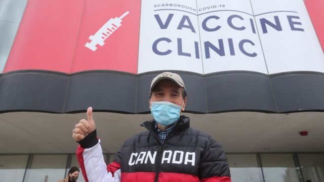 A man in a Canada jacket showing thumbs up at a vaccine centre