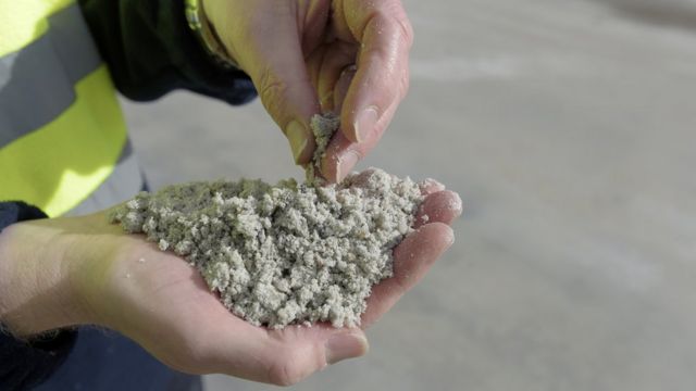 Mão segurando uma espécie de pó, com aparência de areia de praia