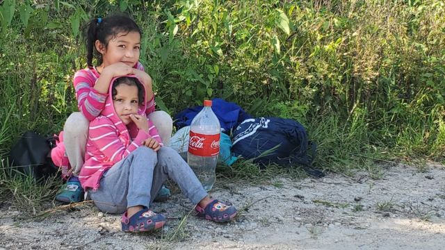Duas crianças migrantes sentadas à beira da estrada