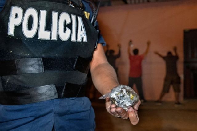 Un policía costarricense muestra una bolsa que contiene dosis de marihuana y crack incautadas durante una operación de búsqueda de drogas en un barrio periférico de San José, Costa Rica, el 30 de julio de 2021.
