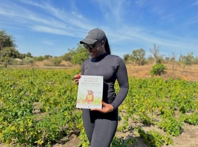 Claudia in her field proudly shows off her book on agricultural planning. 