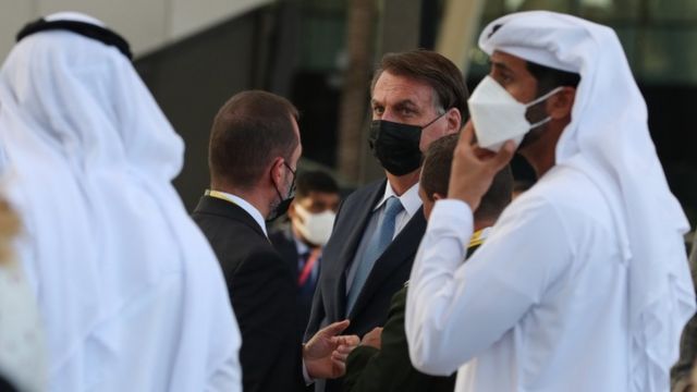 Bolsonaro dans un masque, parmi des hommes en costumes typiques des EAU
