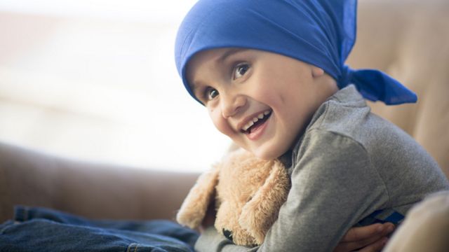 Niña con un pañuelo en la cabeza abrazando un muñeco de peluche