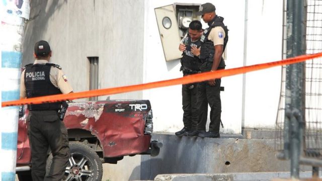 Policías observan un vehículo explotado en Ecuador.