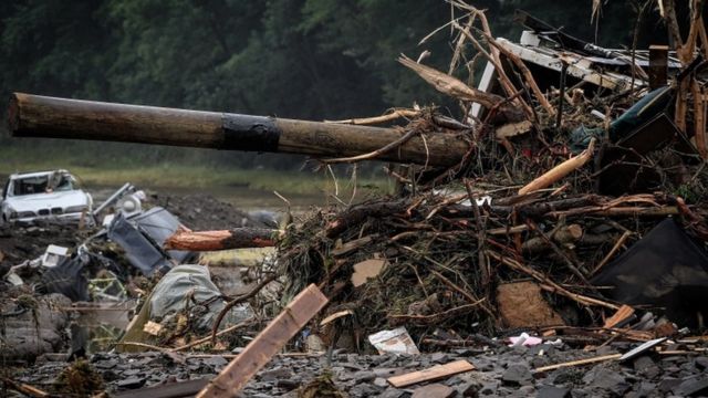 Destroços e pedaços de madeira amontoados perto de carro quebrado