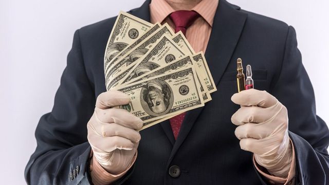 Um homem usando luvas de látex, segurando vacinas em uma mão e dinheiro na outra