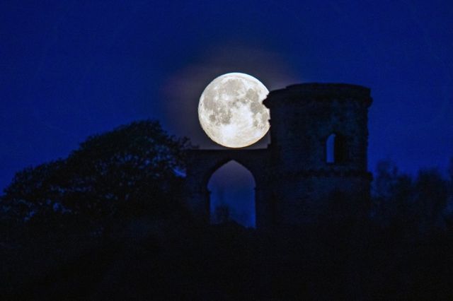 The pink supermoon seen against the silhouetted Mow Cop Folly in Cheshire, UK
