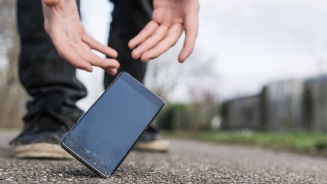 Un teléfono celular cae el suelo mientras unas manos intentan sujetarlo