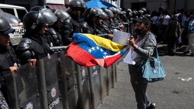 Una trabajadora de la salud frente a un cordón de seguridad de la policía antidisturbios en Caracas.