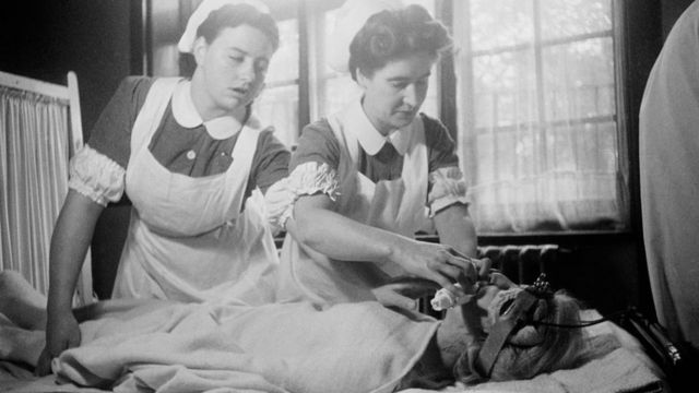 Duas enfermeiras aplicando l terapia com eletrochoque em um paciente