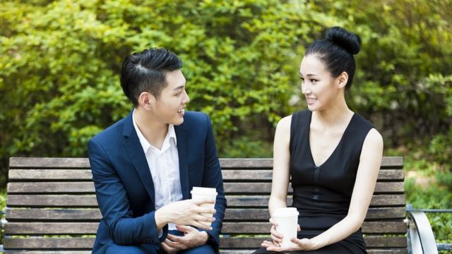 A young couple having coffee on a park bench.