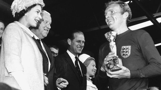 La reina Isabel II entre la Copa Mundial al futbolista inglés Bobby Moore.