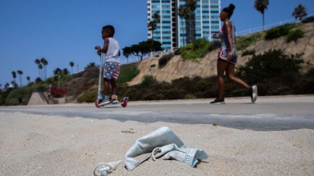 Una mujer y un niño paseando en Long Beach, California, mientras se ve una mascarilla en el piso.