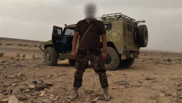 A Wagner soldier stands in front of an armoured vehicle