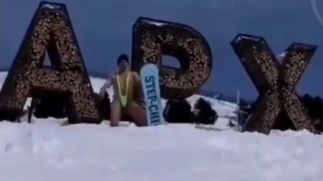 Homem praticando snowboard em uma encosta com um "mankini" estilo Borat