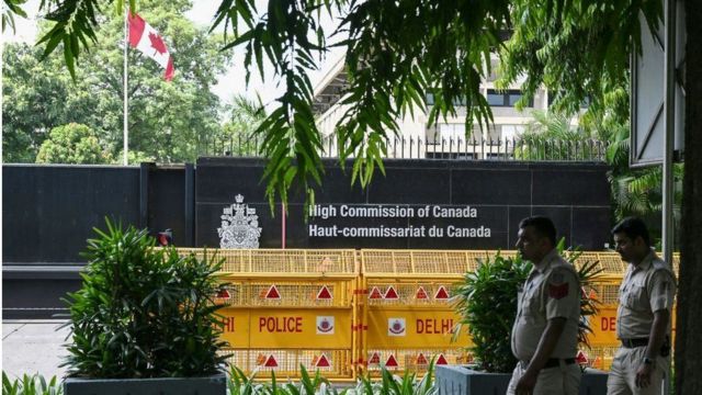 Dois seguranças em frente a portão com nome e brasão do Canadá