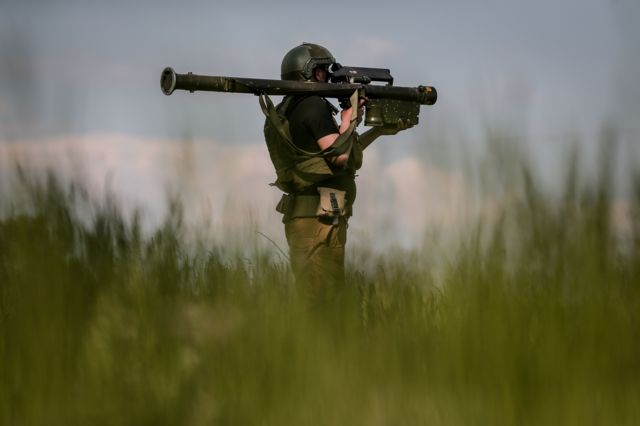 Soldado em pé e de perfil segurando armamento pesado