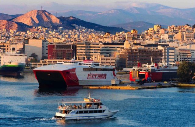 Panoramic view of Piraeus, Greece at sunset showing small and large ferries and mountains in the background