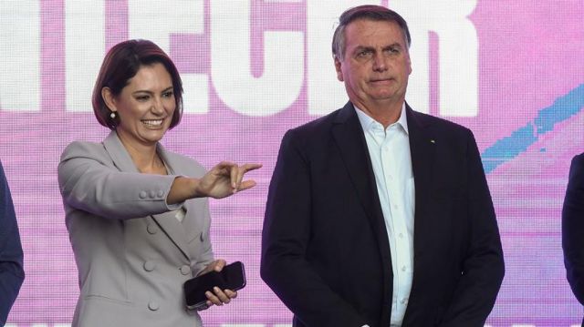 Michelle e Jair Bolsonaro em frente a telão em evento