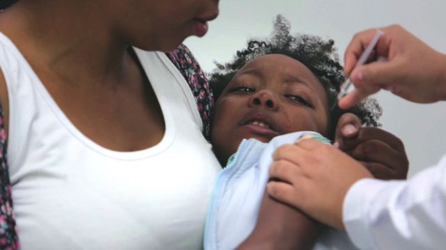 Criança chora no colo da mãe enquanto recebe dose de vacina