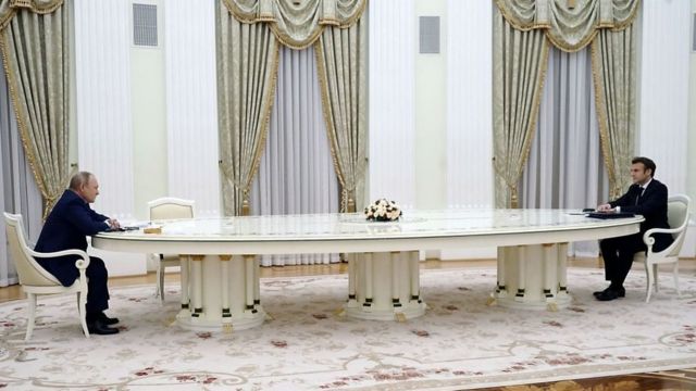 Putin y Macron sentados a los extremos de una larga mesa.