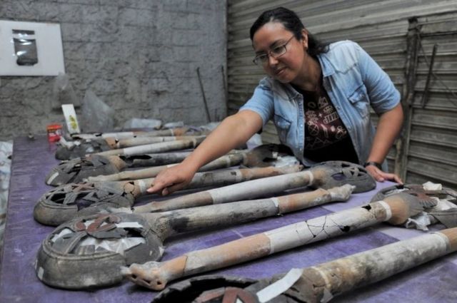 Bir arkeolog kazıda bulunan uzun ve delikli tütsü kaplarını sergiliyor