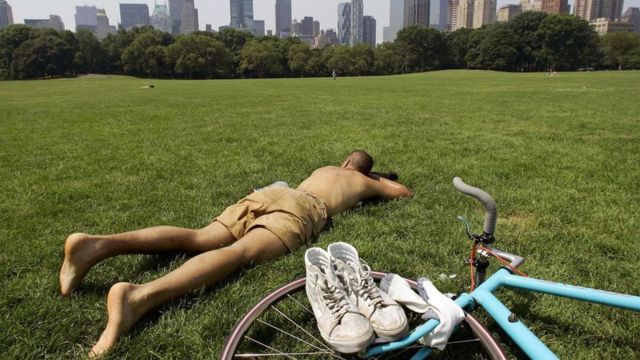 Homem deitado na grama de um parque com bicicleta ao lado