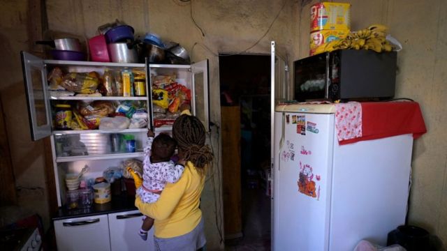 A woman with her son in her arms looks for food in the cupboard.