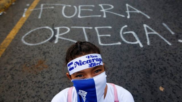 Manifestante delante de una pinta que dice Fuera Ortega.