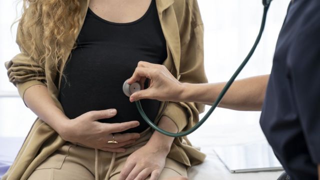 Mujer embarazada es verificada por un médico con un estetoscopio.
