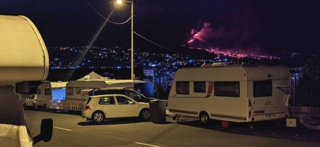 The homeless watch the eruption at night from their caravans.