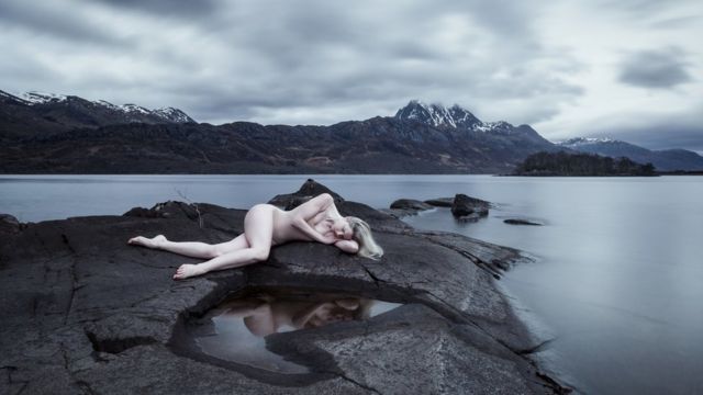Foto de mujer desnuda sobre una roca en un lago.