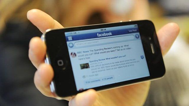 Hand holds phone using Facebook app