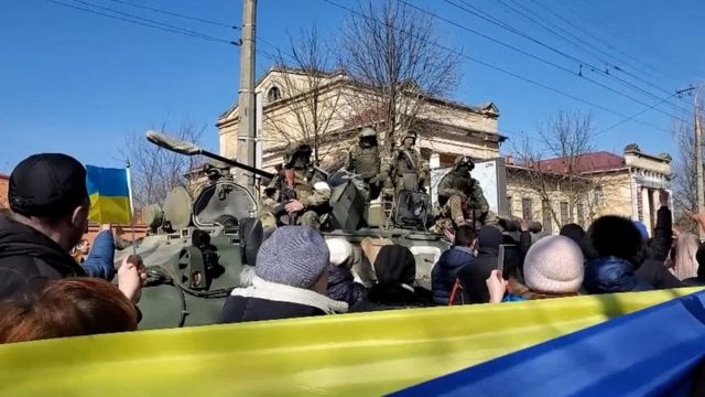 معترضان طرفدار اوکراین در جریان تظاهرات در خرسون از کنار سربازان روسی عبور می‌کنند