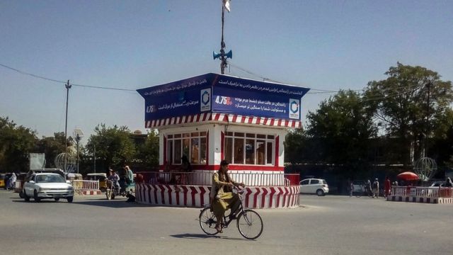 In this picture taken on August 9, 2021 a cyclist rides past a booth with a Taliban flag in the main square of the northern city of Kunduz