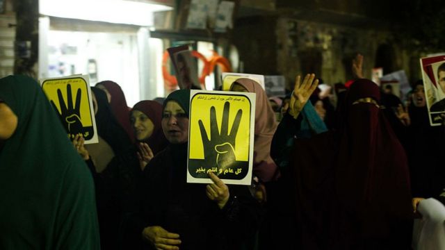 أشخاص يحملون ملصقات للرئيس المصري السابق محمد مرسي وشعار رابعة العدوية أثناء الاحتجاج على النظام في الذكرى الخامسة للثورة المصرية في 2011، في الجيزة