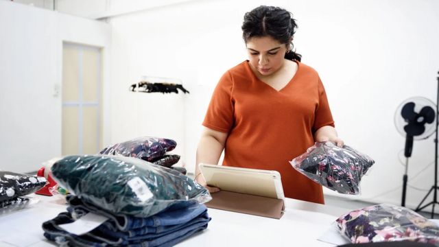 Mulher trabalhando com camiseta na mão enquanto usa tablet