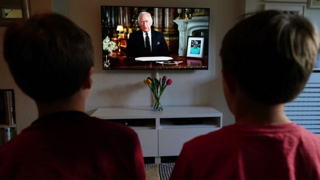 Unos niños miran en televisión el discurso del nuevo rey.